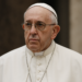 Portrait of Pope Francis in his white cassock and pectoral cross, looking solemnly forward against a softly blurred background.